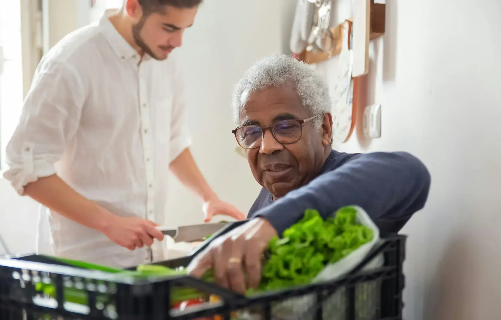 A caregiver assisting an elderly parent with meal preparation in a bright kitchen